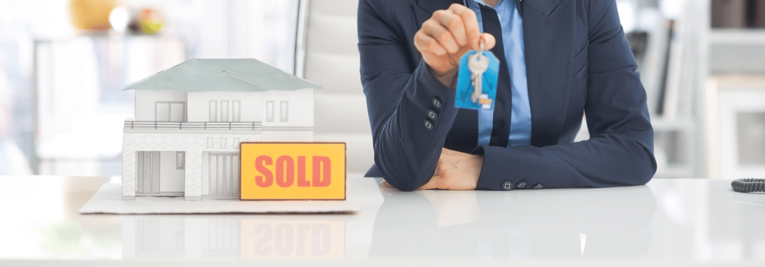 agent holding keys model house and sold sign next to them
